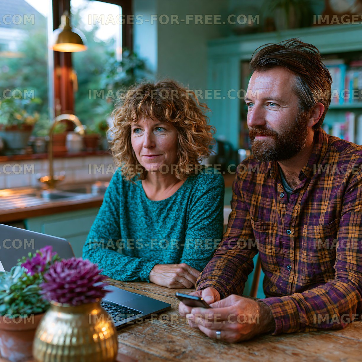 Couple using a laptop and smartphone at a kitchen table