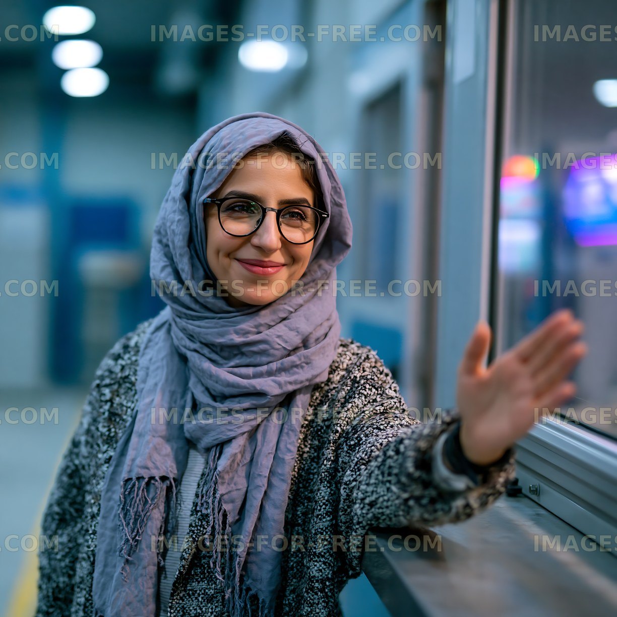 Woman in a gray scarf smiling and waving indoors