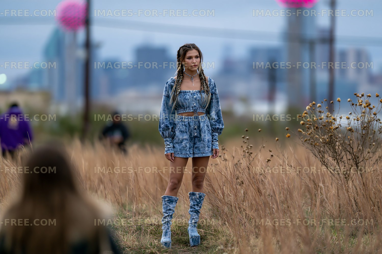 Young woman in denim outfit standing in a field with city skyline