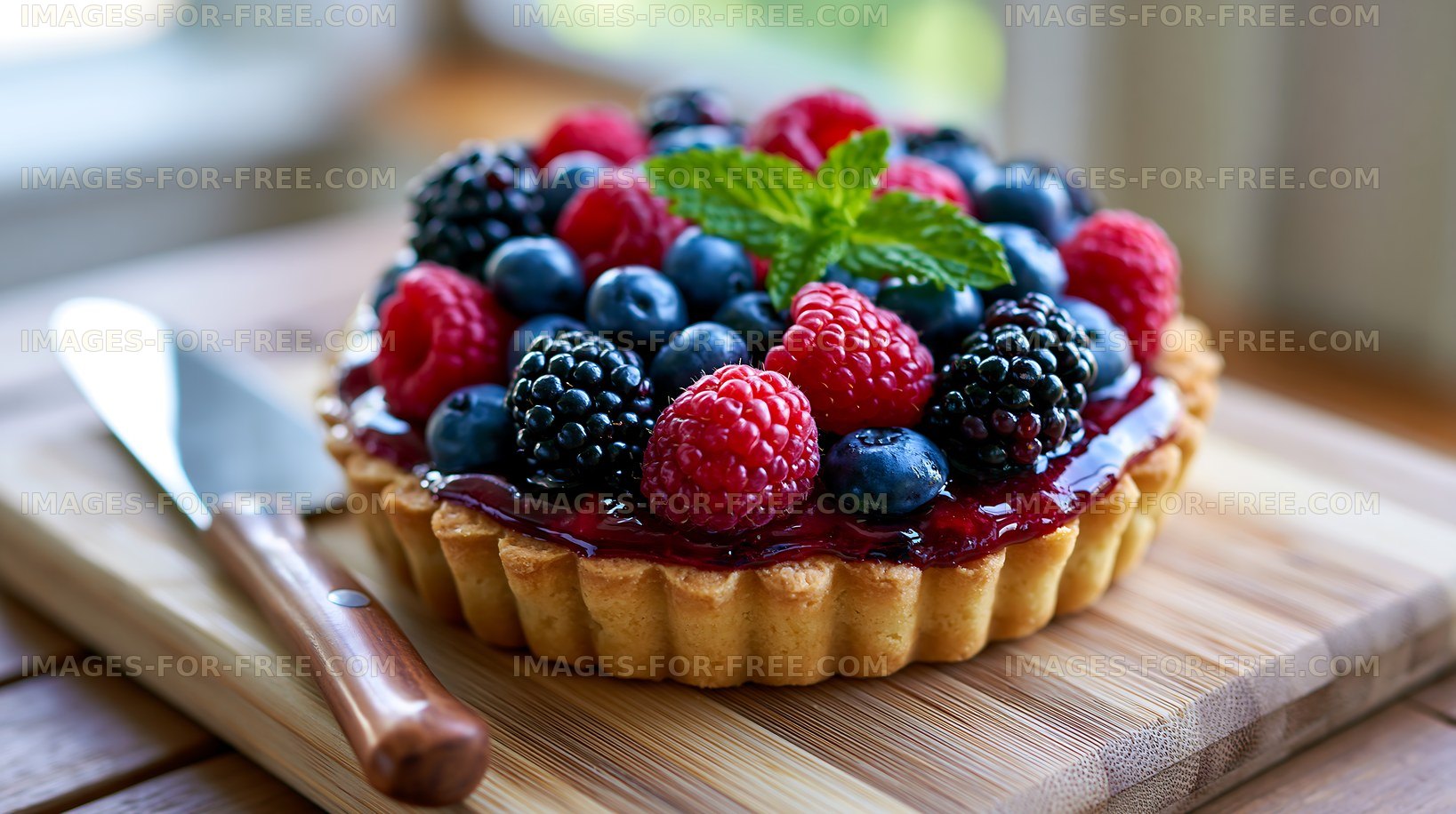 Berry tart on wooden board with knife and fresh mint leaf