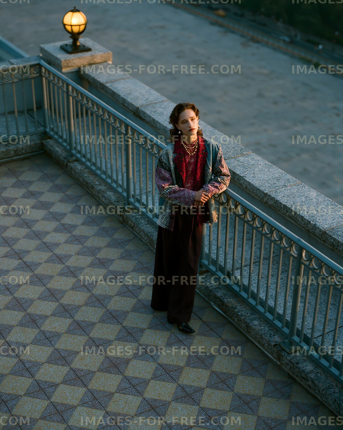 Woman standing on a balcony overlooking a city street at sunset