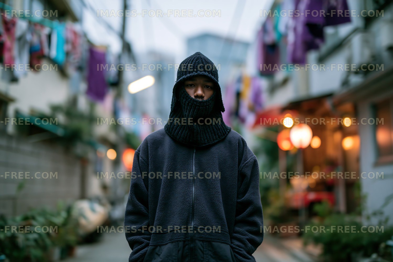 Person wearing a black knit mask stands in a narrow urban street