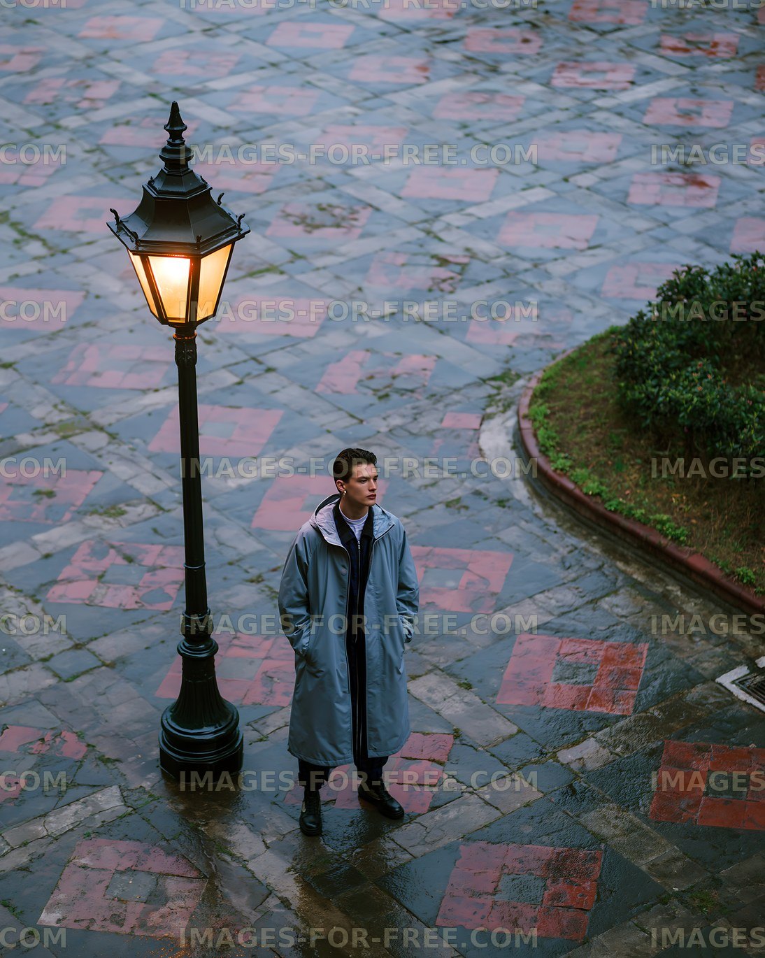 Man standing by street lamp on wet pavement during rainy weather