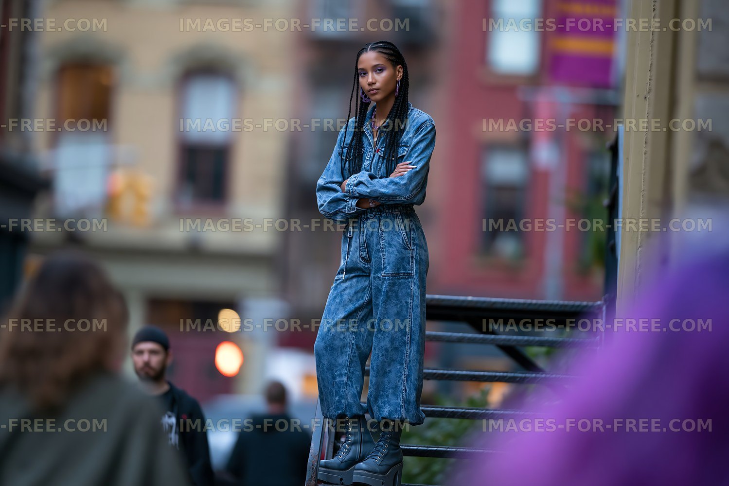 Young woman in denim jumpsuit stands on stairs in urban area