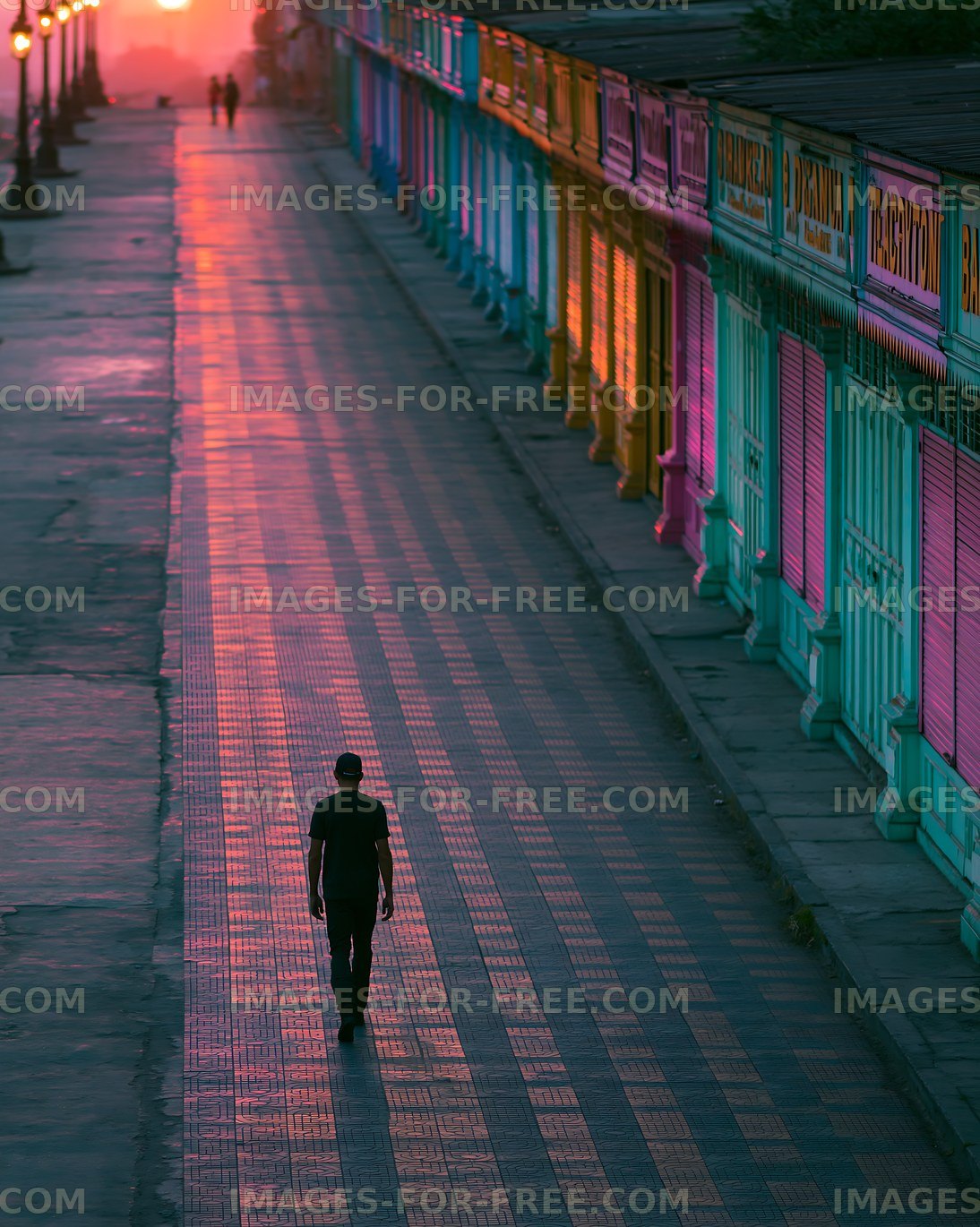 Person walking on a quiet street at sunset with colorful shops