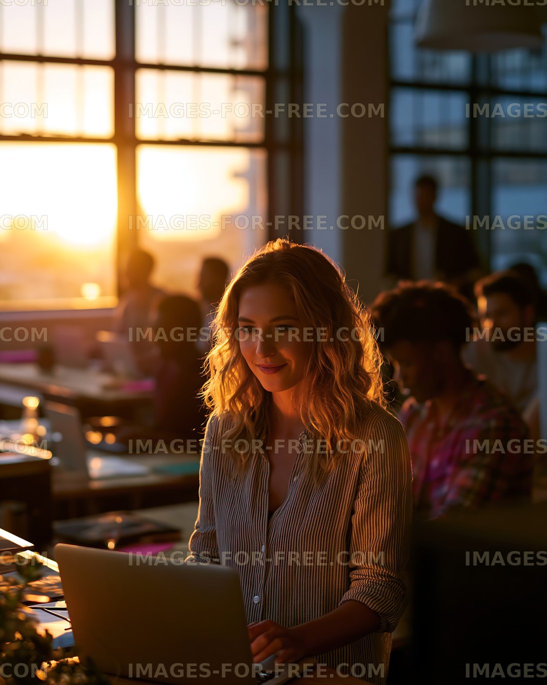Working at a laptop during sunset in a busy office environment