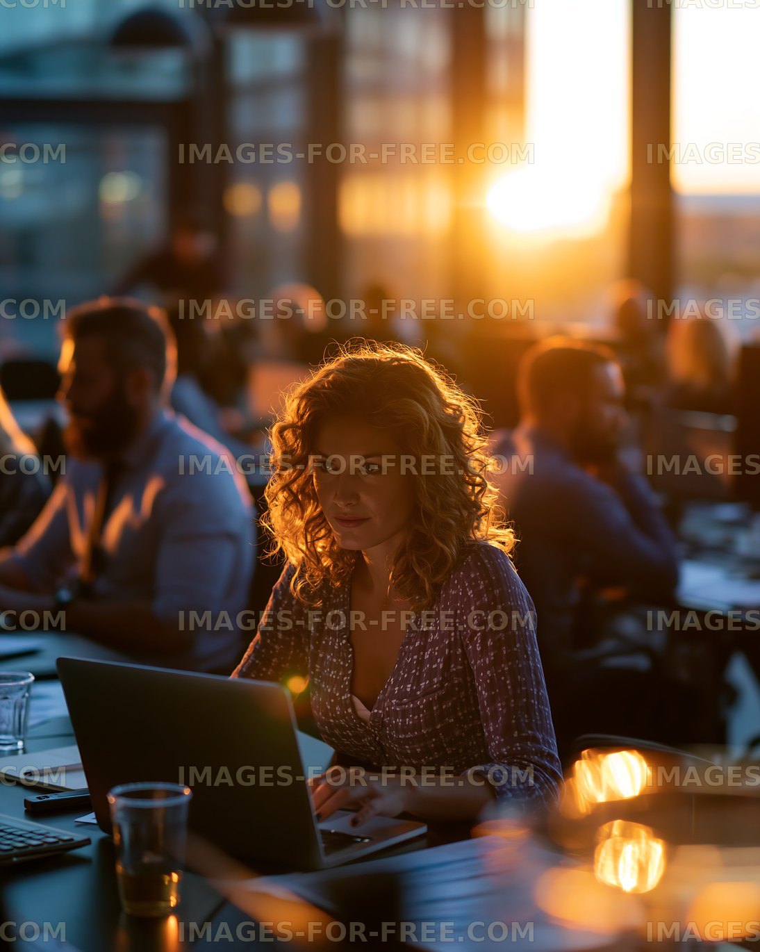 Woman working on laptop in a busy cafe during sunset