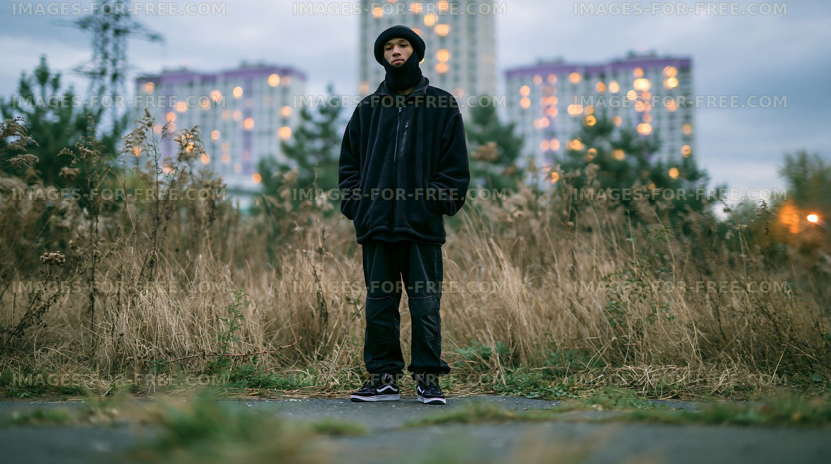 Person standing in tall grass near buildings at dusk