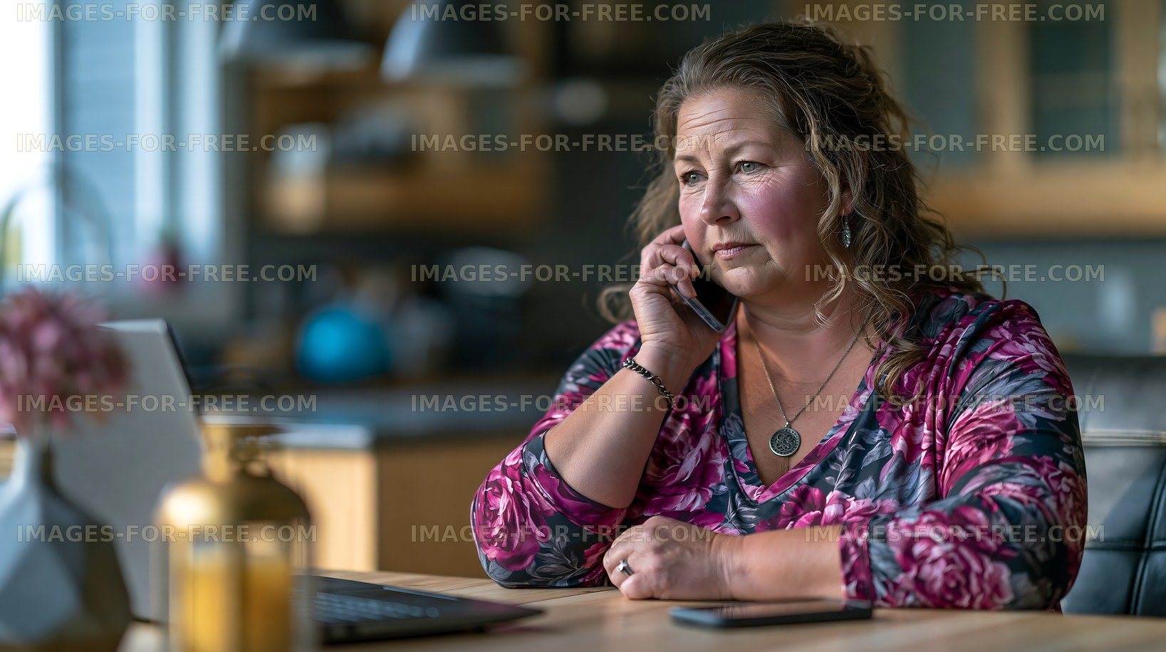 Woman talking on the phone while sitting at a table with a laptop