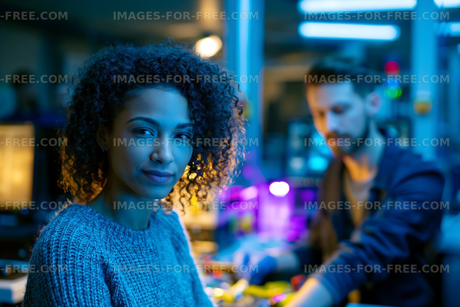 Young woman looks at camera while man works in background