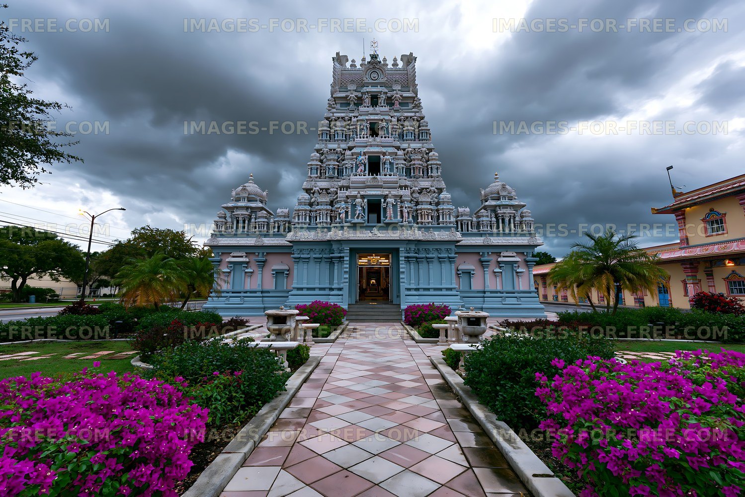 Ornate Hindu temple with flower-lined walkway and stormy sky