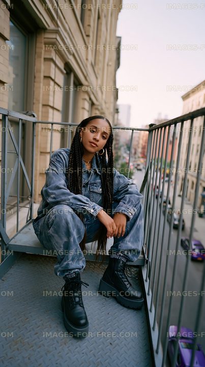 Young woman sitting on balcony wearing denim outfit in urban setting