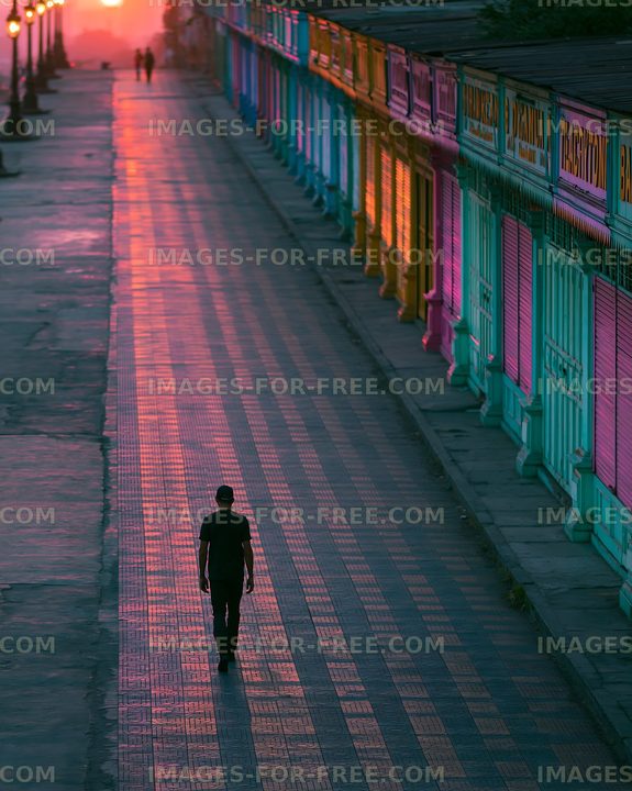 Person walking on a quiet street at sunset with colorful shops