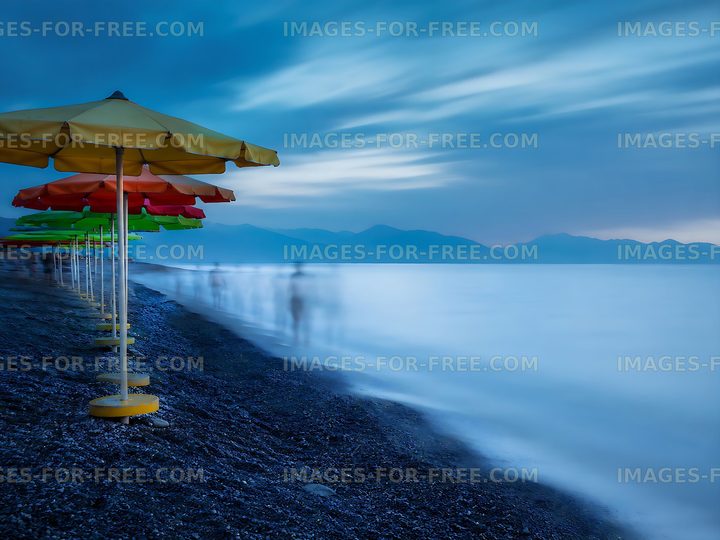 Beach umbrellas by the sea at dusk with blurred figures