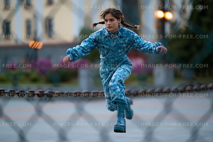 Young person jumping in a blue outfit during evening in a park